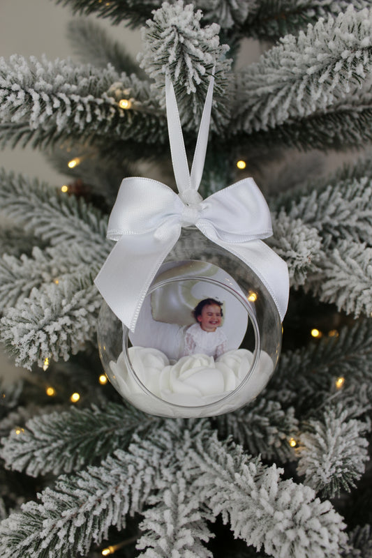 Decorative glass ornament with a white ribbon and a photo of a child inside, surrounded by white flowers.